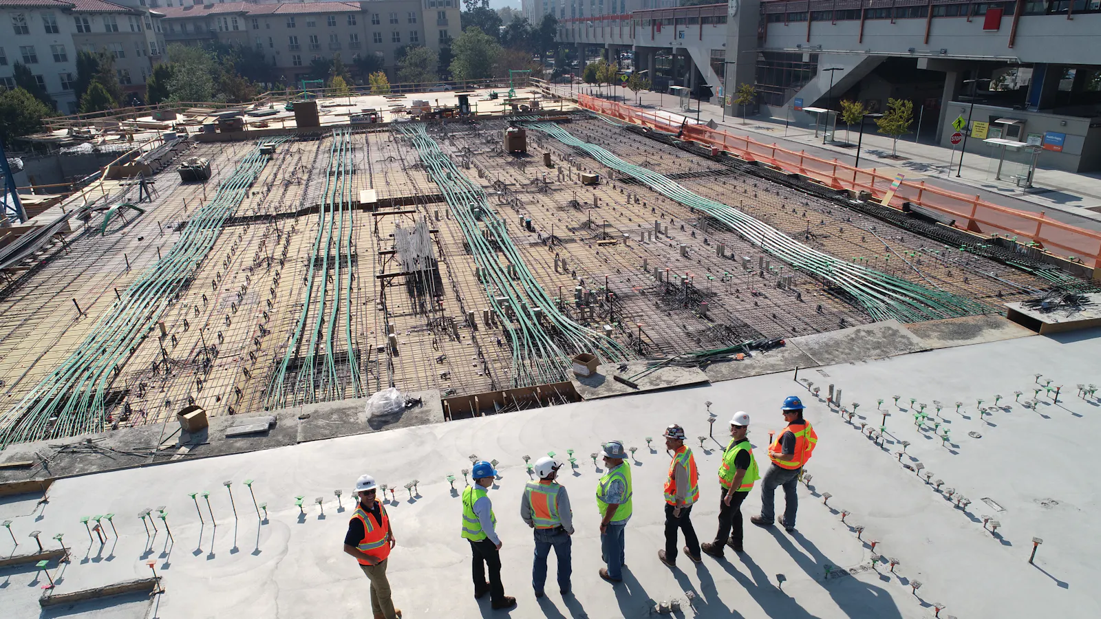 Aerial view of a construction crew standing on a freshly poured concrete slab beside reinforced steel decking